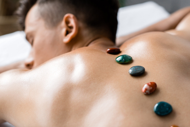 selective focus of shirtless man with colorful stones on his back - Foto, afbeelding