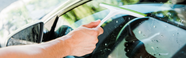 panoramic shot of man holding squeegee while cleaning car window  - Photo, Image