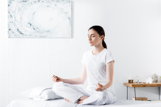 Frau sitzt mit geschlossenen Augen auf Massagetisch in Lotus-Pose - Foto, Bild
