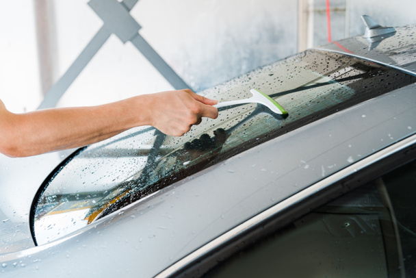 обрізаний вид автомийки, що тримає зачіску та чистить вікно мокрого автомобіля
  - Фото, зображення