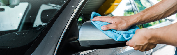 panoramic shot of man cleaning wet car mirror with blue rag  - Fotografie, Obrázek