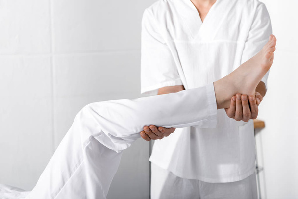 vista cortada de massagista em pé perto da mulher e tocando sua perna
 - Foto, Imagem