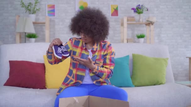surprised and upset african american woman with an afro hairstyle unpacks the parcel,wrong size - Video