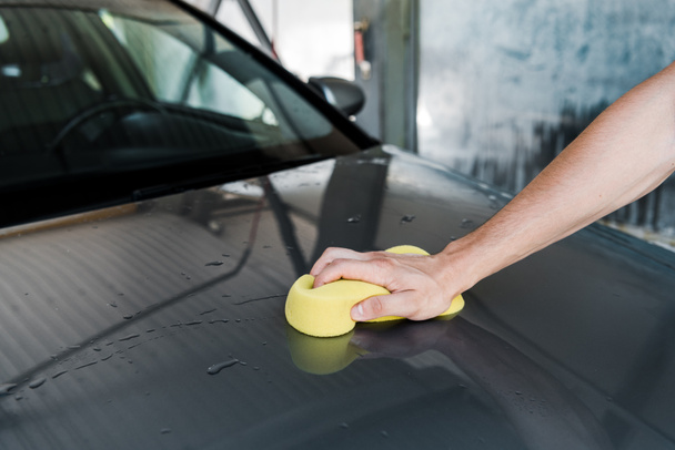araba temizlerken sarı sünger tutan adamın kırpılmış görünümü  - Fotoğraf, Görsel