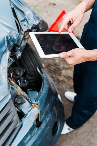 Ausgeschnittene Ansicht eines Mannes, der mit dem Finger auf ein digitales Tablet mit leerem Bildschirm in der Nähe eines beschädigten Autos zeigt  - Foto, Bild