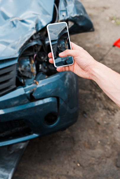 Ausgeschnittene Ansicht eines Mannes mit Smartphone und leerem Bildschirm in der Nähe beschädigter Autos  - Foto, Bild