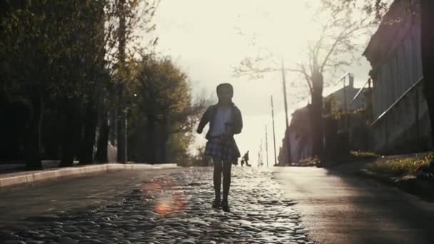 ein neunjähriges Mädchen mit Zöpfen rennt in der untergehenden Sonne zum Pripryshku auf der Straße aus Kopfsteinpflaster. - Filmmaterial, Video