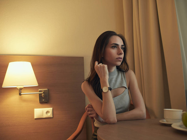 A young brunette is sitting at a table in the hotel room - Фото, зображення
