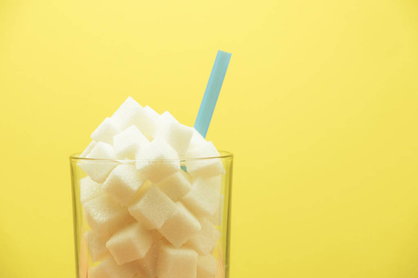 Glass full of cubes sugar with straw on a wooden table  beautiful yellow  background  - unhealthy diet concept. - Photo, Image
