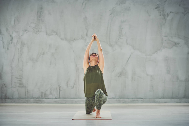 fokussierte charmante kaukasische Brünette in grünem Outfit Kriegerin in Yoga-Pose. - Foto, Bild