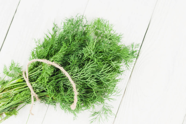 Heap of green fresh raw dill tied of brown rope on old wooden white rustic planks - 写真・画像