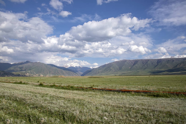 Zielona Dolina, wzgórza i góry z ośnieżonych szczytów na pochmurne niebo. Podróżowanie w Kirgistanie - Zdjęcie, obraz