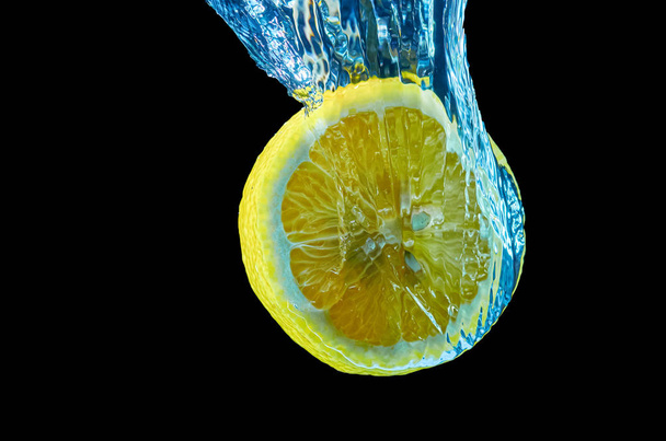 Fresh lemon falling in water with splash on black background - Fotoğraf, Görsel