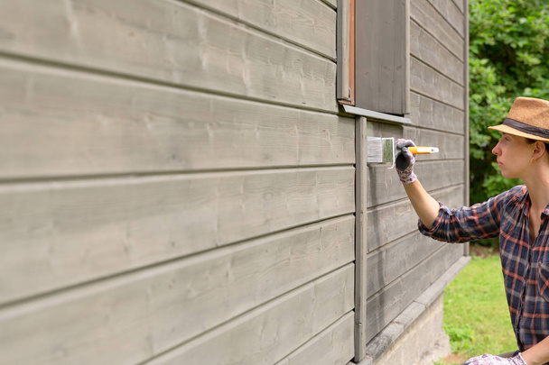Vrouw werknemer schilderij houten huis buiten muur met penseel - Foto, afbeelding