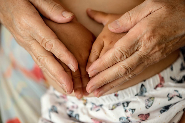 Stare ręce babci trzymania dziecka na jej okrążeniach. Koncepcja generowania rodziny  - Zdjęcie, obraz