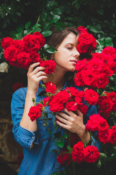 mujer joven cerca del arbusto de rosas rojas en un jardín
 - Foto, imagen