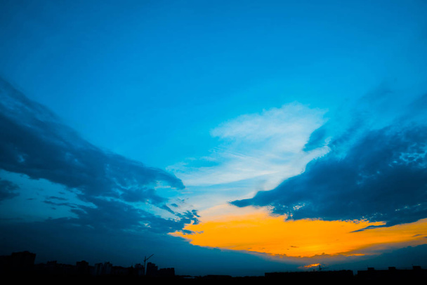 Atmospheric blue cloudy sky behind silhouettes of city buildings. Cobalt and orange background of sunrise with dense clouds and bright yellow sunny light for copy space. Cyan heaven above clouds. - Photo, Image