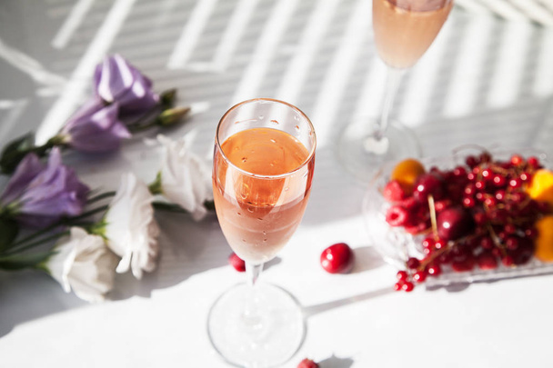 Kieliszki wina różanego na stole obok kwiatów i owoców - Zdjęcie, obraz