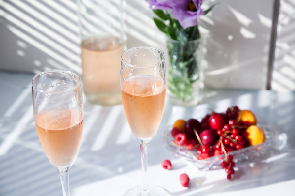 Kieliszki różowego wina na stole obok butelki i owoców - Zdjęcie, obraz