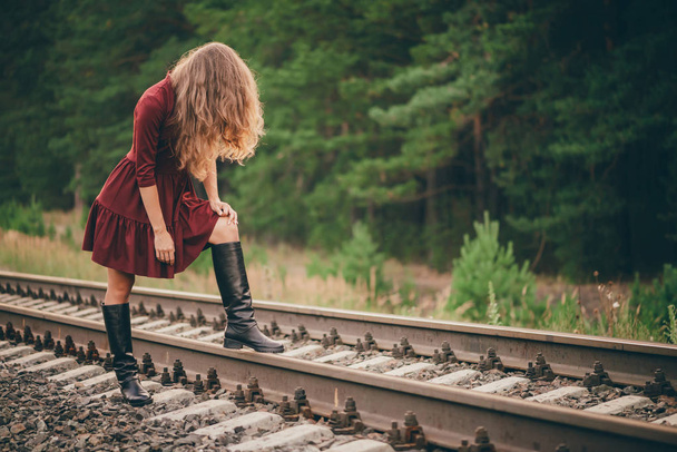 Piękna smutna dziewczyna ukrywa twarz przez włosy. Moody Lady w Burgundii sukienka w lesie na kolei. Depresja samotna dziewczyna na kolej o świcie. Słońce w kręcone włosy naturalne jesienią. Zły nastrój. Obraził dziewczynę. - Zdjęcie, obraz