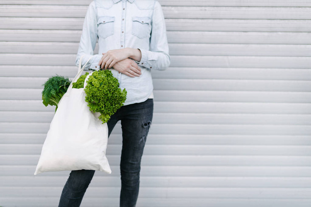 Woman holding an eco bag filled with grocery. Vegetables and fruits are hanging from a bag. Ecology or environment protection concept. White eco bag for mock up. - Fotoğraf, Görsel