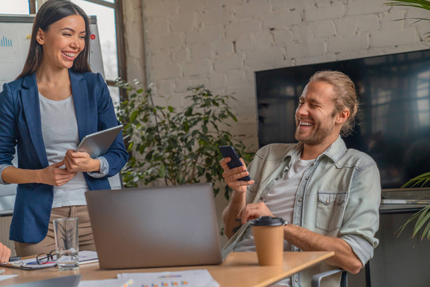 Shot of business professionals laughing while having a meeting in office . Business partners with smartphone in hands having fun in coworking office - Foto, imagen