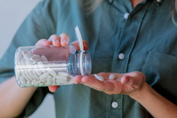 mulher derrama pílulas brancas de um frasco transparente em sua mão
 - Foto, Imagem