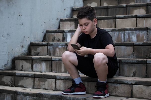 Surullinen poika katselee matkapuhelinta käsin päähän
 - Valokuva, kuva