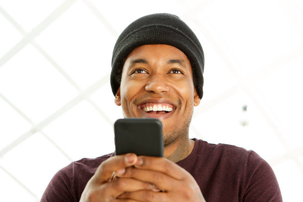 Bliska portret przystojnego afrykańskiego amerykańskiego mężczyzny uśmiechając się i trzymając telefon komórkowy - Zdjęcie, obraz