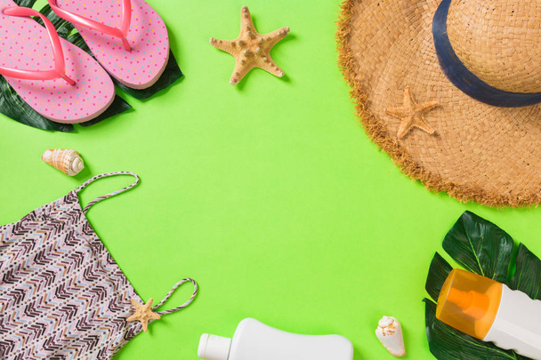 T-shirt, deniz kabukları, flip flop güneş kremi şişesi ve yeşil arka plan üst görünüm düz üzerinde hasır şapka ile Yaz aksesuarları yatıyordu - Fotoğraf, Görsel
