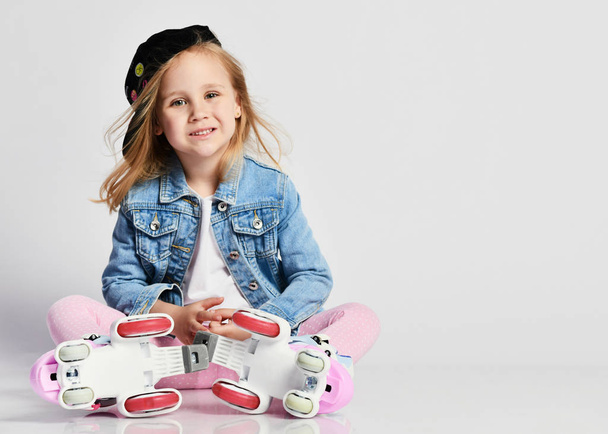 girl sits on the rollers in a blue denim and cap and smiles. Summer sports for children. - Foto, immagini
