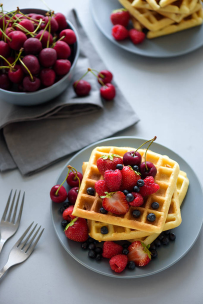 Top view on homemade belgian waffles with berries on gray table. Healthy breakfast concept. - Fotó, kép