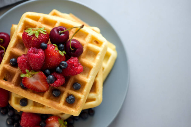 Top view on homemade belgian waffles with berries on gray table. Healthy breakfast concept. - Valokuva, kuva