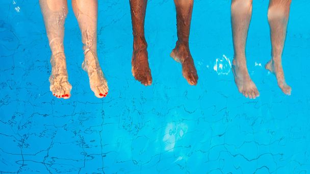 jalat kolmen ystävän (tavalliset ihmiset) eri rotu istuu uima-altaalla aurinkoisena päivänä. Juhlat. Kesällä. Loma, kansainvälinen ystävyys ja urheilu käsite
. - Valokuva, kuva