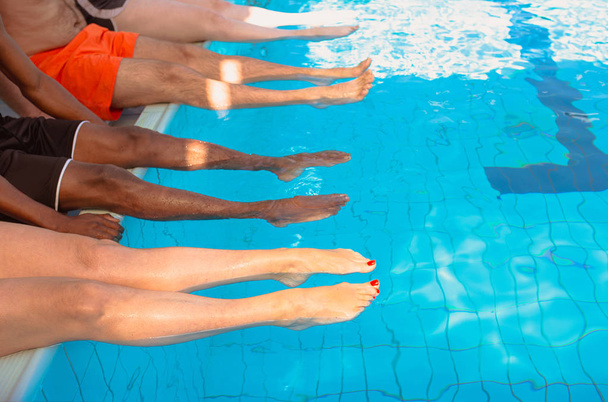 lábak négy barátok (közös emberek) különböző faj ül a medence napsütéses napon. Fél. Nyári. Vakáció, nemzetközi barátság és Sport koncepció. - Fotó, kép