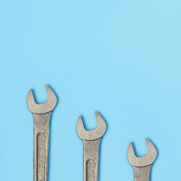 Three metallic spanners lie on texture background of fashion pastel blue color paper - Photo, Image