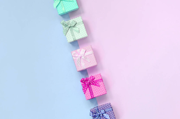 Невеликі подарункові коробки різних кольорів зі стрічками лежать на фіолетовому і рожевому фоні
 - Фото, зображення