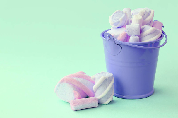 Un secchio di lilla in miniatura pieno di marshmallow giace su uno sfondo verde pastello
 - Foto, immagini