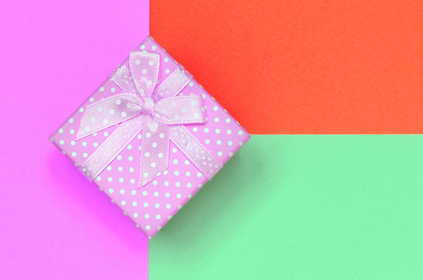 Маленька рожева подарункова коробка лежить на текстурі модного пастельного бірюзового, червоного та рожевого кольорів паперу
 - Фото, зображення