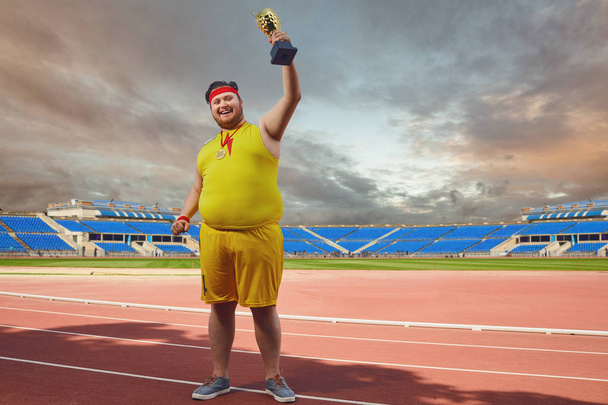 A fat man with a winners cup in his hands at the stadium. - Foto, imagen