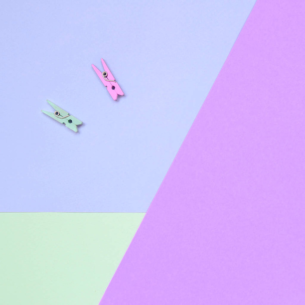 Dwa kolorowe drewniane kołki leżą na tle tekstury mody pastelowe fioletowe, turkusowe i różowe kolory papieru - Zdjęcie, obraz