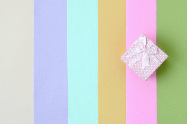 Pequeña caja de regalo rosa se encuentran en el fondo de textura de los colores pastel de moda rosa, azul, verde, amarillo, violeta y beige
 - Foto, Imagen