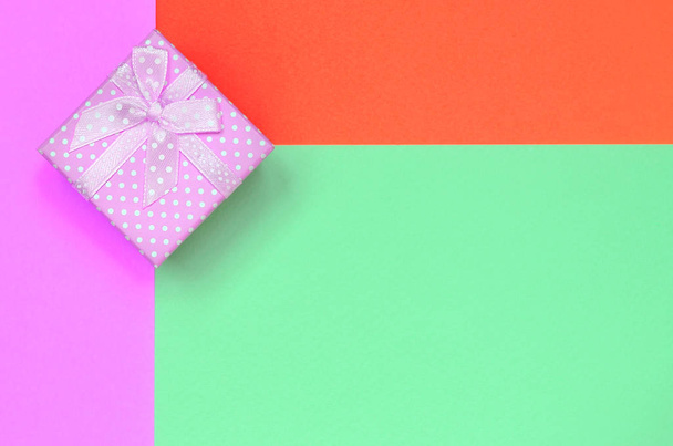 Malá růžová Dárková krabice leží na pozadí texturové tyrkysové, červené a růžové barvy papíru - Fotografie, Obrázek