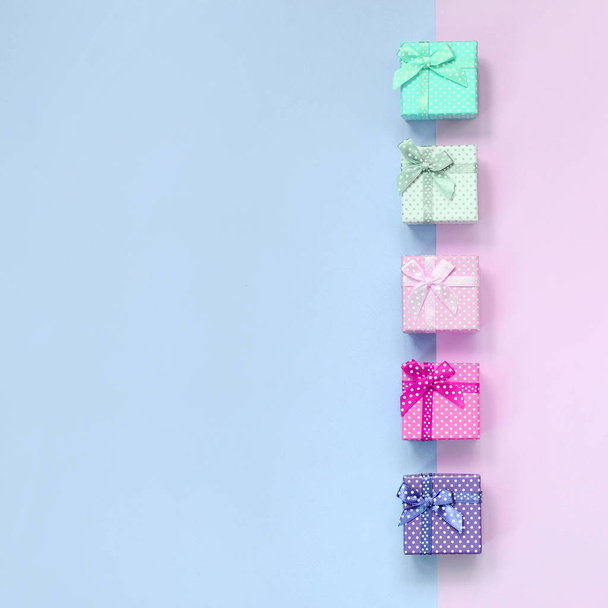 Невеликі подарункові коробки різних кольорів зі стрічками лежать на фіолетовому і рожевому фоні
 - Фото, зображення
