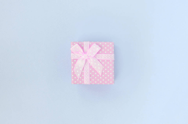 Маленька рожева подарункова коробка зі стрічкою лежить на фіолетовому фоні
 - Фото, зображення