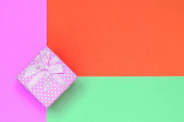 Маленька рожева подарункова коробка лежить на текстурі модного пастельного бірюзового, червоного та рожевого кольорів паперу
 - Фото, зображення