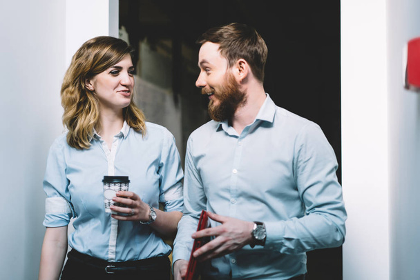 Two smiling office workers in formal wear enjoying communication during coffee break, cheerful male and female colleagues laughing from funny joke on business subject in modern company interior - Foto, Bild