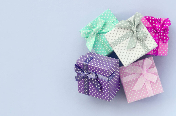 Куча маленьких цветных подарочных коробок с лентами лежит на фиолетовом фоне
 - Фото, изображение