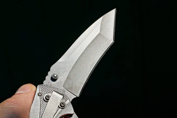 un cuchillo plegable gris en la mano sobre fondo negro
 - Foto, imagen