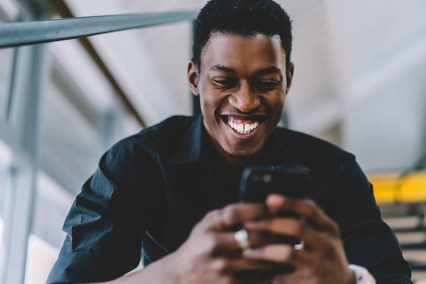 Cheerful excited black man reading positive news in social network using 4g connection on modern cellphone, happy dark skinned male watching funny comedy content via application on smartphone - Foto, afbeelding